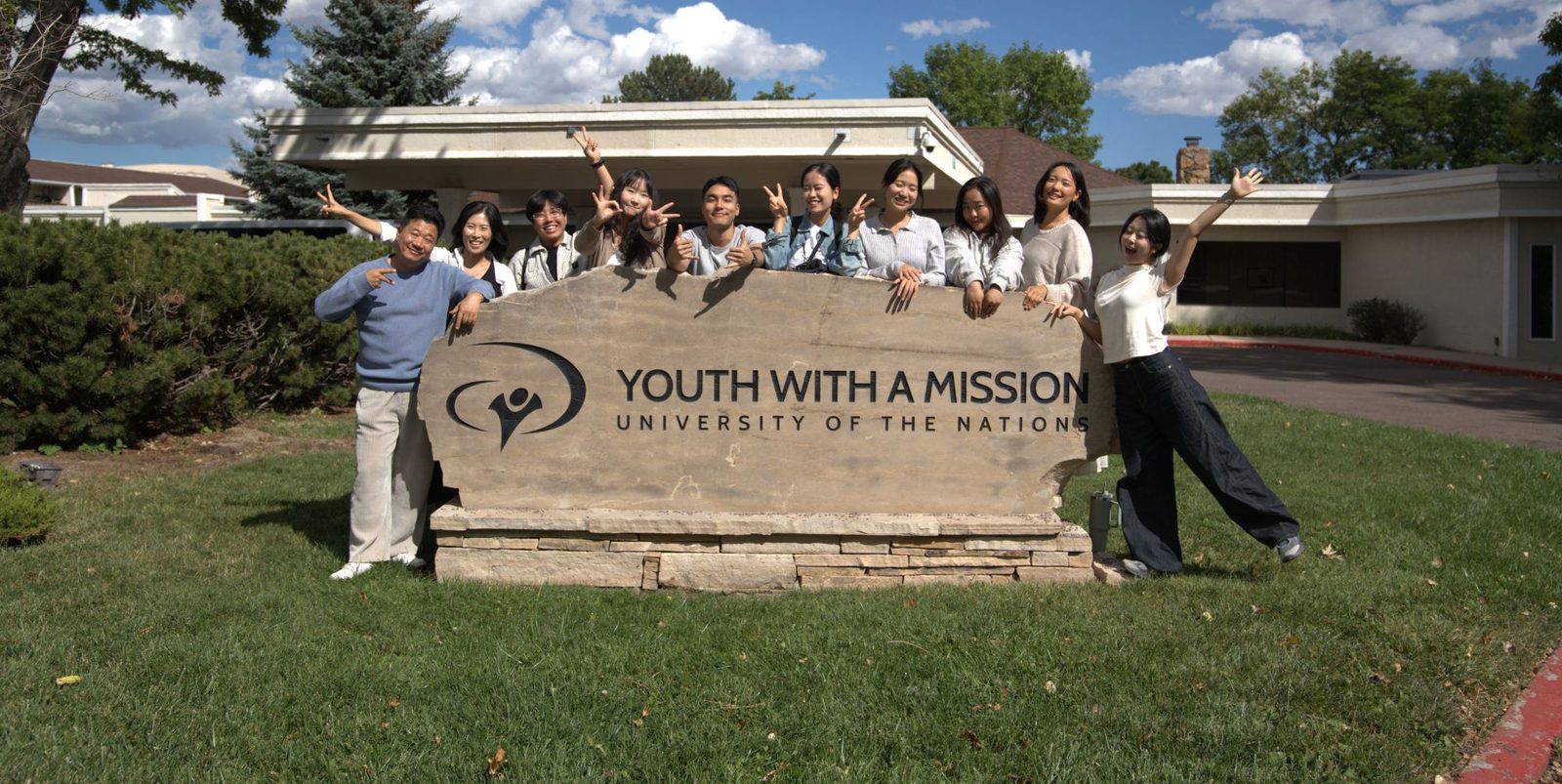 One Korea DTS students and staff waving behind the Youth With A Mission, University of the Nations sign in Colorado Springs