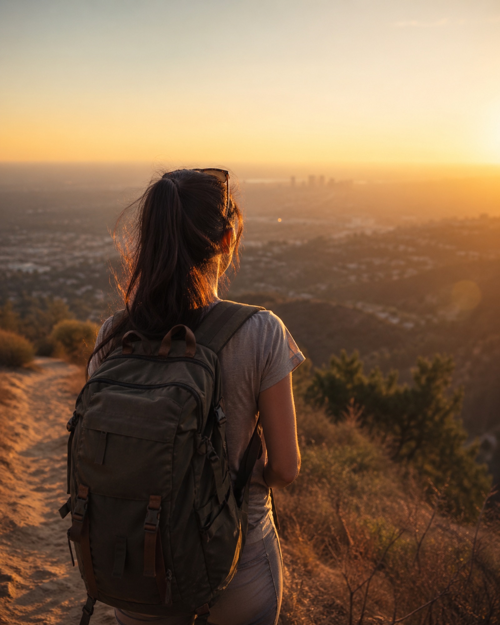A traveler at golden hour, looking out over a city in the valley below.